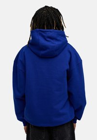 Blauer Pullover-Hoodie mit einer vorderen Tasche, dickem Stoff, oversized Passform, Kordelzugkapuze und gerippten Bündchen. Die Rückansicht zeigt kein Logo.