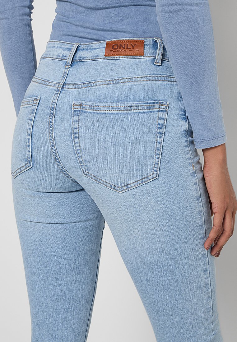 Hellblaue Jeans aus Denim mit einer figurbetonten Passform, zwei Gesäßtaschen und einem braunen Lederschild am Bund. Weicher Stoff und klassische Nähte.