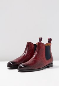 Bottines en cuir rouge à motif crocodile avec des panneaux élastiqués sur les côtés et des tirettes, présentant une finition brillante et une semelle plate.