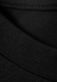 O tecido de algodão preto apresenta uma textura ribeteada com costuras e pregas suaves, destacando a sua suavidade e leveza.