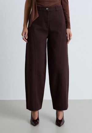 Donna che indossa pantaloni a vita alta marrone scuro a gamba larga con cuciture frontali e décolleté bordeaux scuro con punta a stiletto.