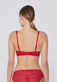 Sostenes de encaje rojo con tirantes ajustables, bordes festoneados y cierre de gancho y ojal. Diseño ajustado con detalles de patrón intrincado en la tela.