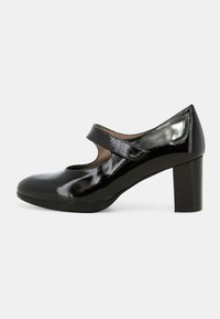 Scarpa nera in vernice con tacco alto, punta rotonda, cinturino alla Mary Jane e tacco spesso e testurizzato. Superficie liscia con una leggera lucentezza.