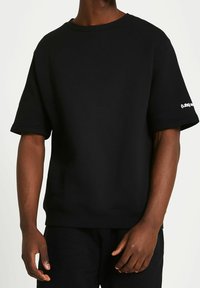 Black sweatshirt featuring a round neck and short sleeves. Made from soft fabric with a relaxed fit. Displays logo detail on the left sleeve.