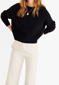 Czarny sweter z dzianiny o luźnym kroju z prążkowanymi mankietami, zestawiony z kremowymi spodniami o szerokich nogawkach. Posiada okrągły dekolt i teksturowany wzór.
