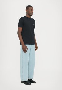 Svart bomullströja med korta ärmar och rund hals; har en liten vit logotyp på vänster bröst. Tillsammans med ljusblå vida jeans.