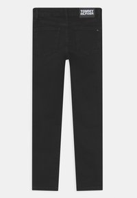 Jeans de mezclilla negra con un corte slim, que cuentan con dos bolsillos traseros y una etiqueta con el logo de Tommy Hilfiger en la cintura, textura suave y diseño limpio.