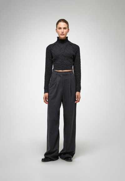 Zwarte cropped kabelgebreide trui met een hoge kraag, gecombineerd met donkergrijze wijde broek. Gladde textuur en op maat gemaakte pasvorm.