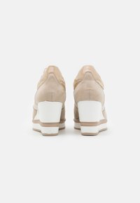 Beige suede and glossy patent leather sneakers with a white wedge heel, featuring a smooth texture and contrasting light accents.