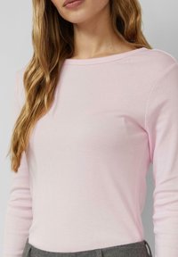 Lichtroze shirt met lange mouwen en een boothals, gemaakt van zachte stof; heeft een eenvoudig ontwerp zonder zichtbare patronen of accenten.