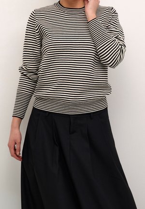 Pull tricot à rayures noires et blanches avec des manches longues et un col rond, porté avec un pantalon noir plissé taille haute.