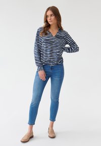 Top de rayas en azul marino y blanco de manga larga con escote en V, combinado con jeans ajustados de color azul claro y zapatos de lona beige.