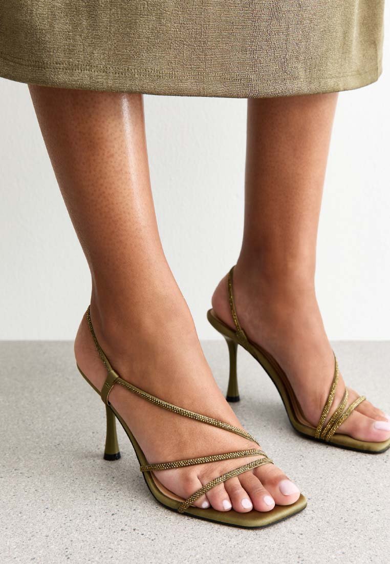 Olivgröna klacksandaler med tunna remmar, med metalliska detaljer och en fyrkantig tådesign på en platt yta.