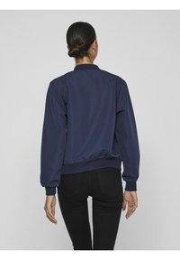 Mörkblå bomberjacka med ribbad krage och muddar. Tillverkad av ett slätt material och har en åtsittande midjeresår.