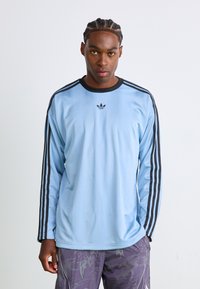 Light blue long-sleeve athletic shirt with black accents and three black stripes on each sleeve. Features a small black logo on chest.