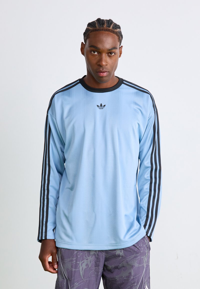 Light blue long-sleeve athletic shirt with black accents and three black stripes on each sleeve. Features a small black logo on chest.