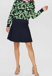 Zielony sweter w kwiatowy wzór z różowym dekoltem, zestawiony z dopasowaną granatową spódnicą i beżowymi sandałami na słupku.