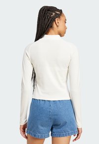 Long-sleeve, cream top with a fitted design, raglan sleeves, and a rounded neckline, paired with blue denim shorts. Smooth texture.