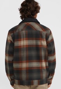 Plaid särgid musta, halli ja roostevärvi, valmistatud kudumiskangast. Omab kraed ja nööpidega mansette. Tagantvaates on nähtavad õmblustead.