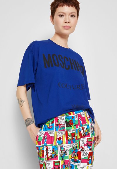 Camiseta de algodão azul com texto preto "MOSCHINO COUTURE Milano" acompanhada de calças estampadas com tema de banda desenhada, apresentando várias ilustrações coloridas.