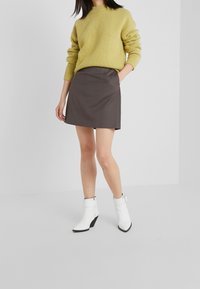 Pull en tricot jaune, jupe grise avec poches, et bottines blanches à talon compensé noir. Design simple et moderne.