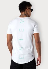 White short-sleeve t-shirt featuring vertical mint green text on the back. Soft cotton material with a rounded hem and relaxed fit.