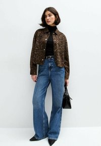 Jacke mit Leopardenmuster, schwarzer Rollkragenpullover, hoch taillierte, ausgestellte blaue Jeans, schwarze Handtasche, schwarze spitze Absätze. Glatter Stoff, lässige Passform.