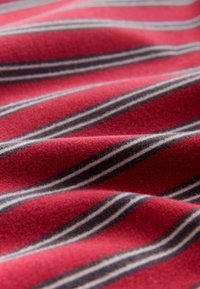 Punane kangas pehme tekstuuriga, millel on horisontaalsed triibud mustas ja valges. Muster loob materjalil lainelise välimuse.