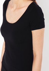 T-shirt noir ajusté à manches courtes et encolure dégagée. Fabriqué en coton doux et extensible. Texture lisse avec un design proche du corps.