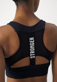 Black sports bra with a mesh back, featuring a wide strap marked "STRONGER." Smooth fabric with reinforced seams and a racerback design.