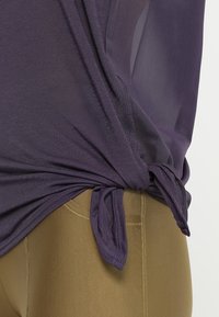 Lila lättviktig topp med knuten sidodetalj, ihopparad med beige leggings med en slät textur och figurnära design.