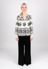 Schwarze und weiße gemusterte Bluse mit langen Ärmeln, die Sonnen- und Blumenmuster zeigt, kombiniert mit weiten schwarzen Hosen. Glatte Textur.