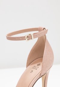 Blassrosa High Heel Schuh mit einem strukturierten Kunstleder-Obermaterial, Knöchelriemen und goldener Schnalle. Mit einer spitzen Zehenform und glatter Innenauskleidung.