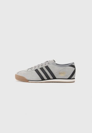 Lysegrå ruskind Adidas sneaker med sorte striber, gummisål og guld Adidas Italia-logo på siden, set fra ydersiden.