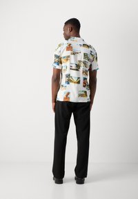 Kortærmet skjorte med hvid bund og farverige fotografiske tryk. Sorte bukser som komplimenterer outfittet. Glat tekstur, afslappet pasform.