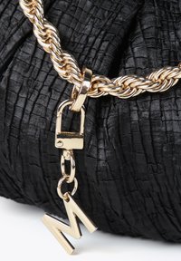 Bolso negro texturizado con una cadena dorada. Presenta un cierre de candado dorado y un charm dorado en forma de "M" colgante.