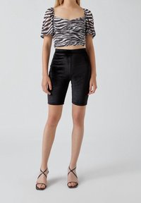 Shorts de vélo taille haute en velours noir accompagnés d'un haut court arborant un motif zèbre en noir et blanc. Sandales noires à lanières.