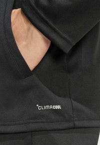 Μαύρη αθλητική μπλούζα με υφή, διαθέτοντας πλαϊνή τσέπη και λευκό λογότυπο "CLIMACOOL" κοντά στο στρίφωμα.