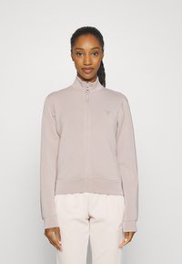 Light pink zip-up jacket with a high collar, ribbed cuffs and hem, featuring a small logo on the chest. Smooth fabric texture.