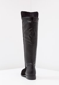 Botas negras hasta la rodilla hechas de cuero suave con un puño de ante, que presentan una puntera redondeada y un tacón bajo y plano.