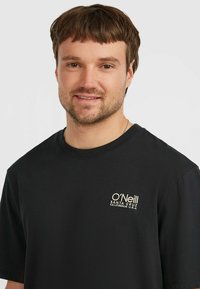 Sort bomulds T-shirt med rund halsudskæring og korte ærmer. Forsiden viser et lille hvidt og gyldent O'Neill-logo med lokationsdetaljer.