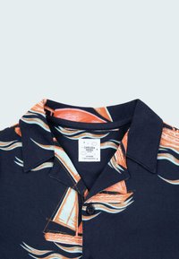 Mörkblå kortärmad skjorta med orange segelbåtar och vågmönster. Kragdesign med knapp, tillverkad av lättvikts tyg.