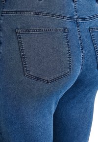 Jeans de denim azul ajustados con una textura suave, cintura alta y un solo bolsillo trasero con costuras en tono. 