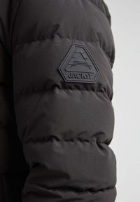 Sort pufferjakke med quiltet tekstur. Har et gummiseret trekantet logo mærke mærket "JACK1T" på den øverste arm.