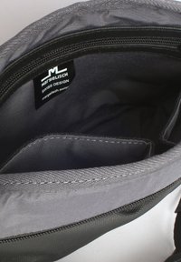Interno di una borsa di tessuto grigia con cerniera, dotata di due scomparti e un'etichetta con la scritta "MARGELISCH SWISS DESIGN" ben visibile. Texture liscia.