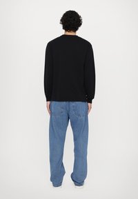 Black long-sleeve shirt with a crew neck, paired with loose-fitting light blue denim jeans, showcasing a relaxed silhouette and casual style.