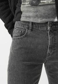 Černé denimové džíny slim fit s přední kapsou, viditelným švem a zapínáním na knoflík. Tkanina má jemnou strukturu a postupné vyblednutí.