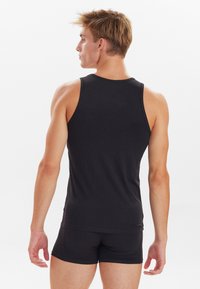 Schwarzes, figurbetontes Tank-Top aus weichem Stoff, mit rundem Halsausschnitt und ärmellosem Design, von hinten an einem Modell präsentiert.