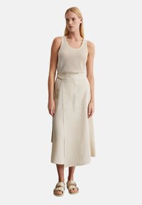 Beige ribbed tank top paired with a wrap-style, cream-colored linen skirt. The outfit is completed with light-colored sandals.