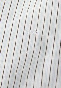 White cotton fabric with blue and brown vertical stripes. Features embroidered white branding on the lower section. Soft texture.